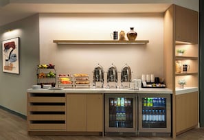 Una colazione a buffet con macchina del caffè, frutta fresca e distributori di bevande.