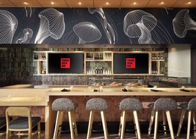 Un bar de sushi con diseño moderno, que cuenta con una barra con taburetes y una exhibición de platos de sushi.