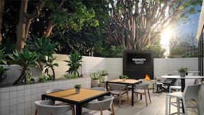 An outdoor patio area with tables and chairs, surrounded by potted plants and a large tree.
