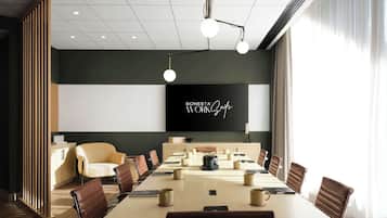 Un salón de conferencias con una larga mesa, sillas de cuero marrón y una gran pantalla que muestra 'SONESTA WORKZone'.