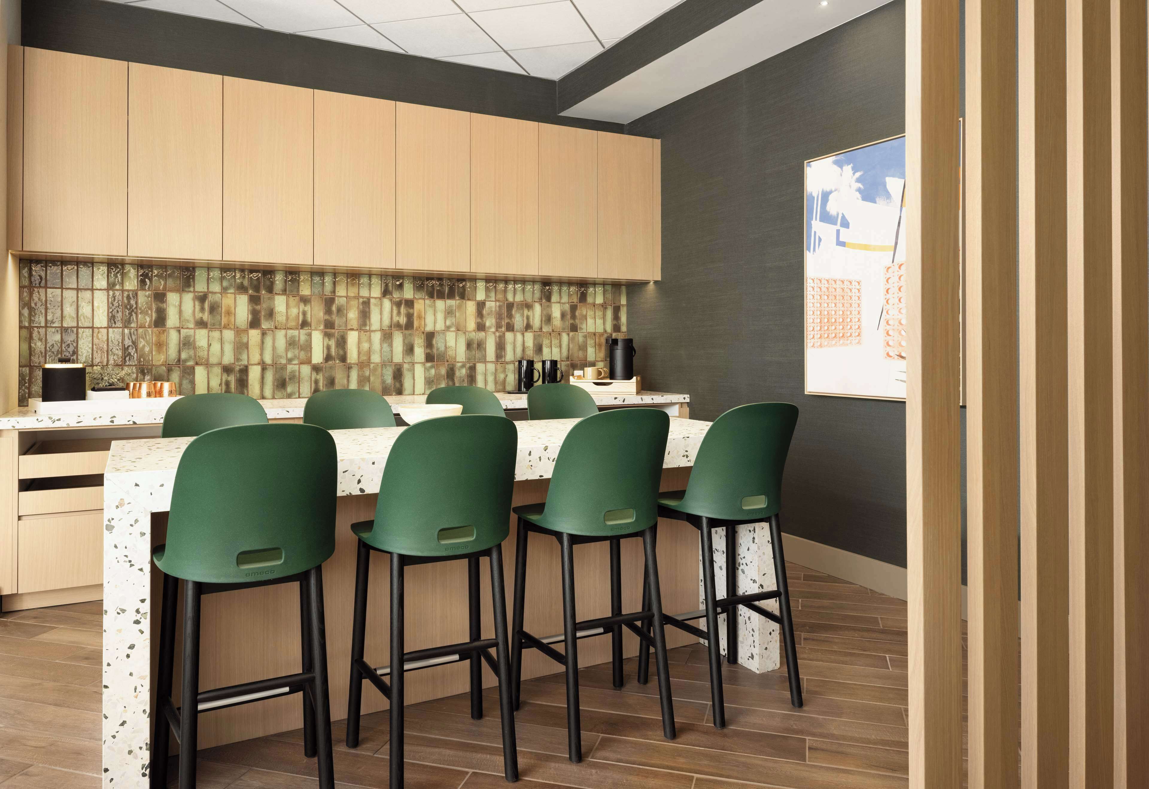 A modern kitchen with wooden cabinets, a tiled backsplash, and a dining area with green chairs and a white table.