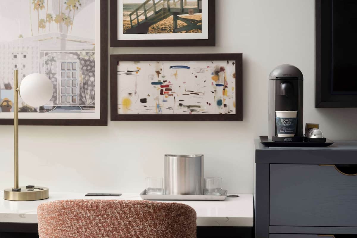 A modern hotel room with a desk, a coffee machine, and framed artwork on the wall.