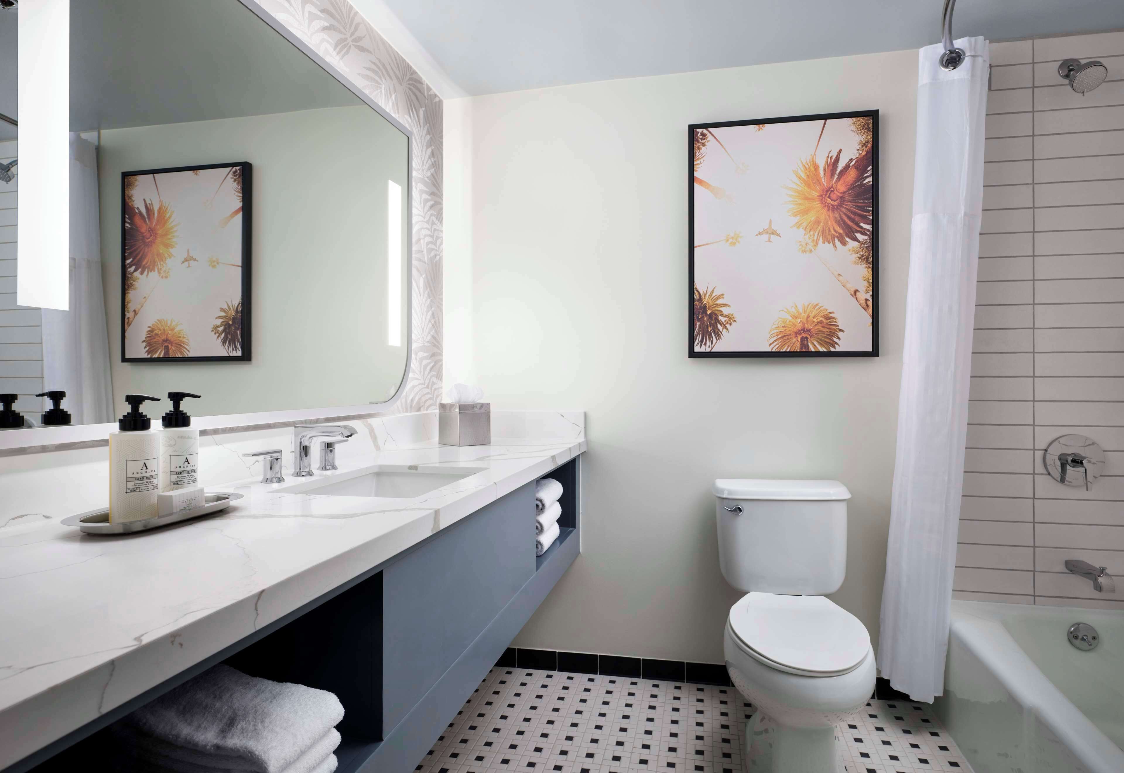 A modern bathroom with a white sink, a toilet, and a shower. There are two framed floral artworks on the wall.