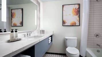 A modern bathroom with a white sink, a toilet, and a shower. There are two framed floral artworks on the wall.
