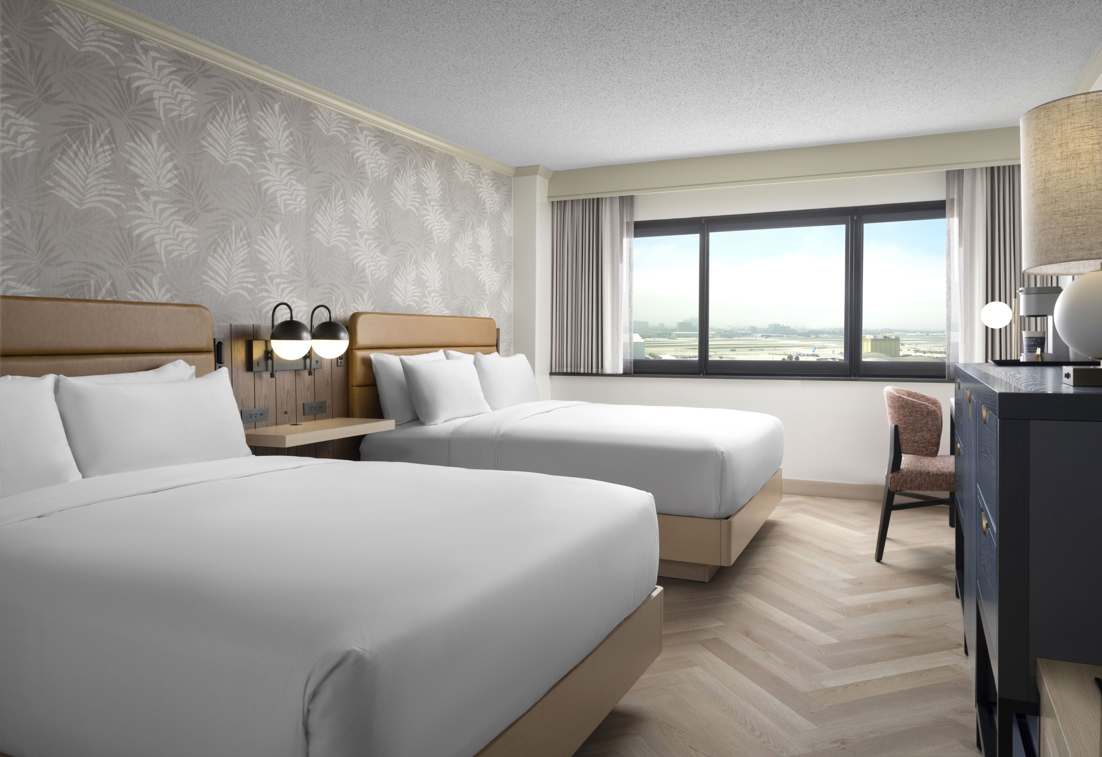 A hotel room with two beds, a desk, a chair, and a large window with a view.