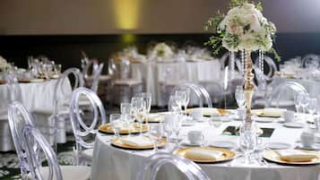Un salón de banquetes con mesas redondas dispuestas para un evento formal, con sillas transparentes y manteles blancos.