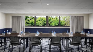 Un salón de conferencias con una larga mesa, sillas y vistas a árboles a través de amplios ventanales.