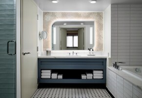 Een moderne badkamer met een grote spiegel, dubbele wastafels, een badkuip en een behang met een patroon.
