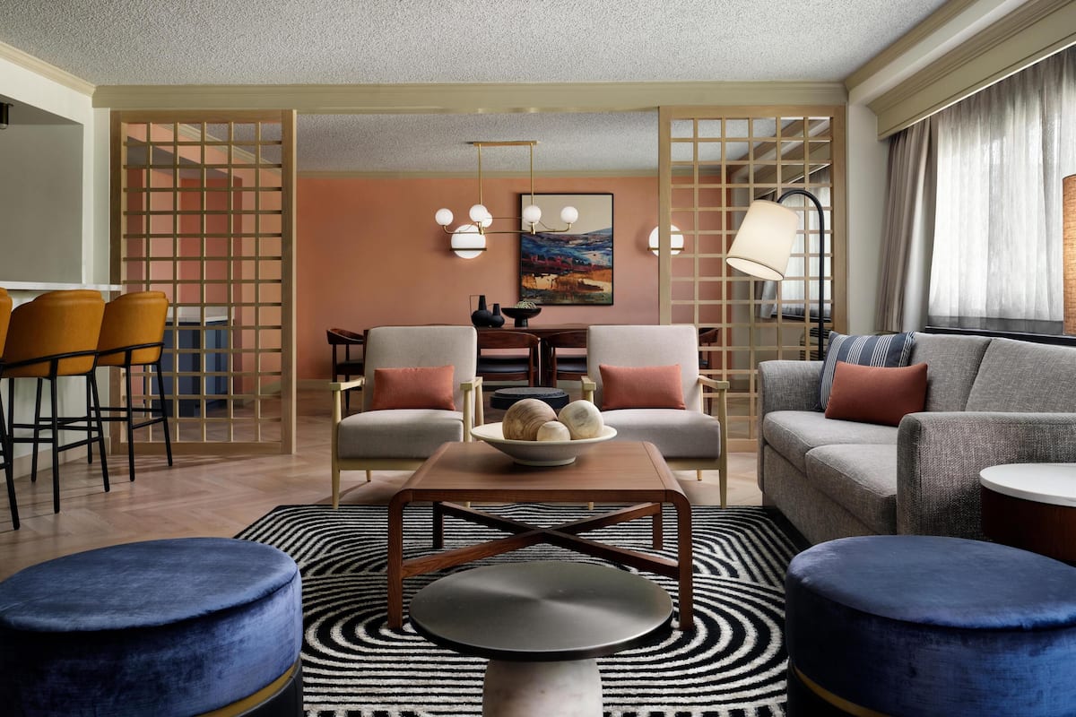 A modern living room with a sofa, armchairs, a coffee table, and a dining area with chairs and a table.