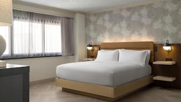 Une chambre d’hôtel moderne avec un grand lit, une tête de lit en bois, deux tables de chevet avec des lampes, une fenêtre avec des rideaux et un papier peint à motifs.