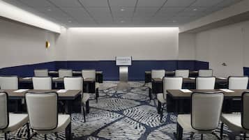 A conference room with rows of tables and chairs, a patterned carpet, and a sign indicating it's part of the Sonesta hotel in Los Angeles Airport.