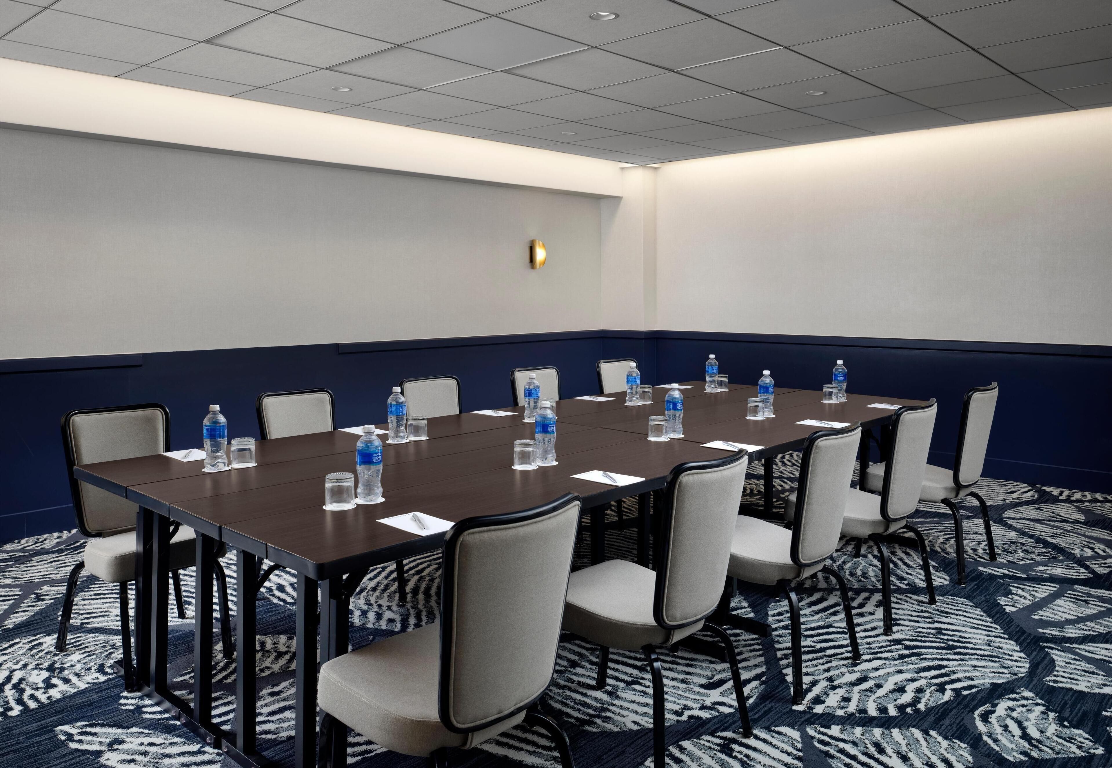 Une salle de conférence avec une longue table, des chaises, des bouteilles d’eau et un tapis à motifs.