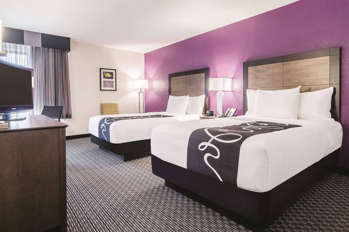 Een hotelkamer met twee bedden, een bureau en een flatscreen-tv, en een groot raam met gordijnen.