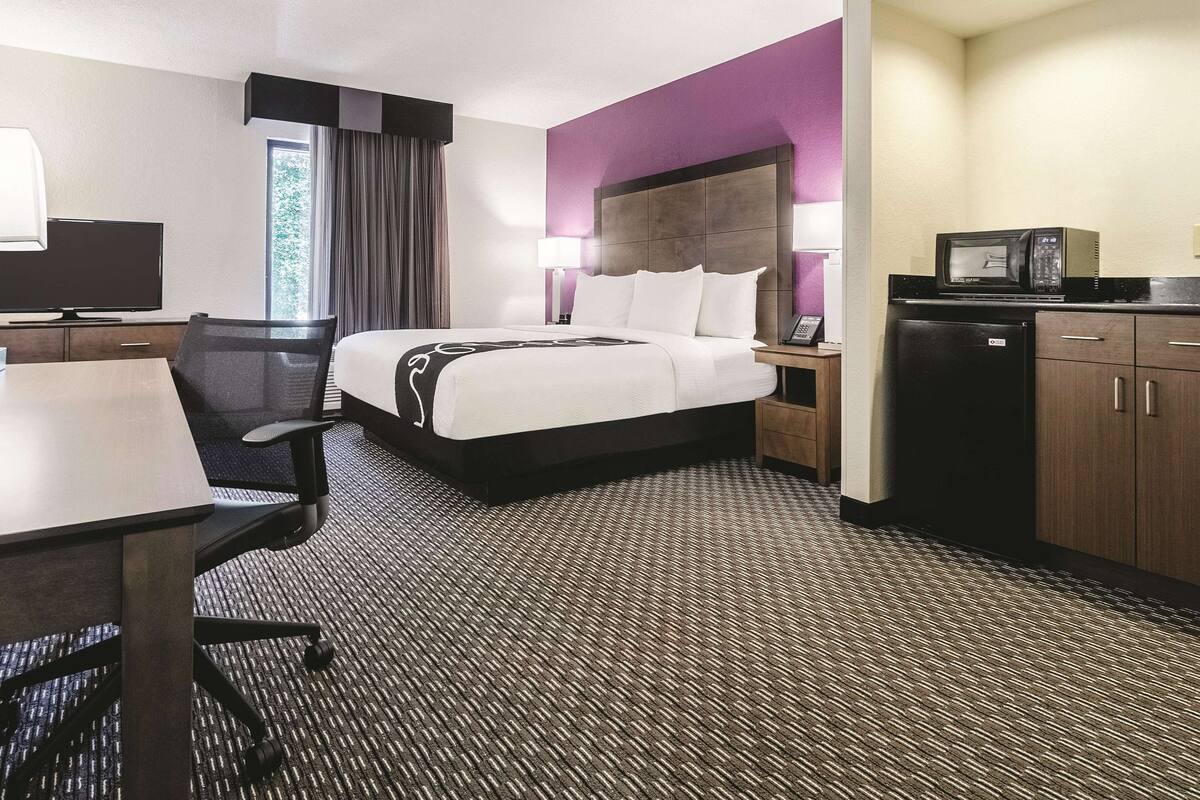 Een hotelkamer met een bed, bureau, stoel en kitchenette.