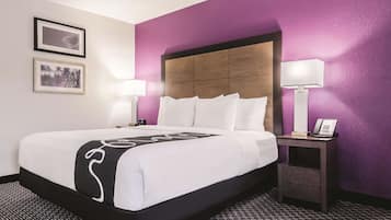 Quarto de hotel com uma cama grande, duas luminárias de cabeceira, mesa de cabeceira com telefone e cabeceira com painel de madeira.