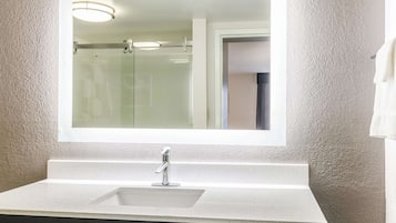 Une salle de bain avec un lavabo blanc, un miroir et une douche visible au fond.