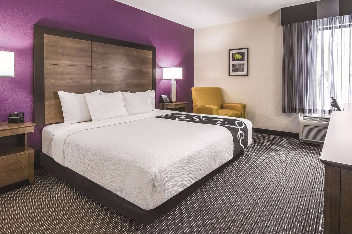 Een hotelkamer met een groot bed, een stoel, een bureau en een raam met gordijnen.