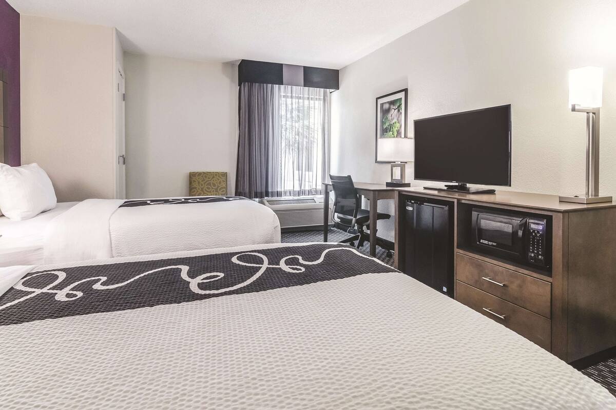Een hotelkamer met een bed, een bureau met een computer, een televisie en een magnetron.