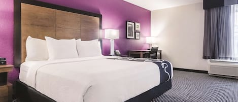 Ein Hotelzimmer mit einem großen Bett, einem Schreibtisch mit Stuhl, einer Lampe und einem Fenster mit Vorhängen.