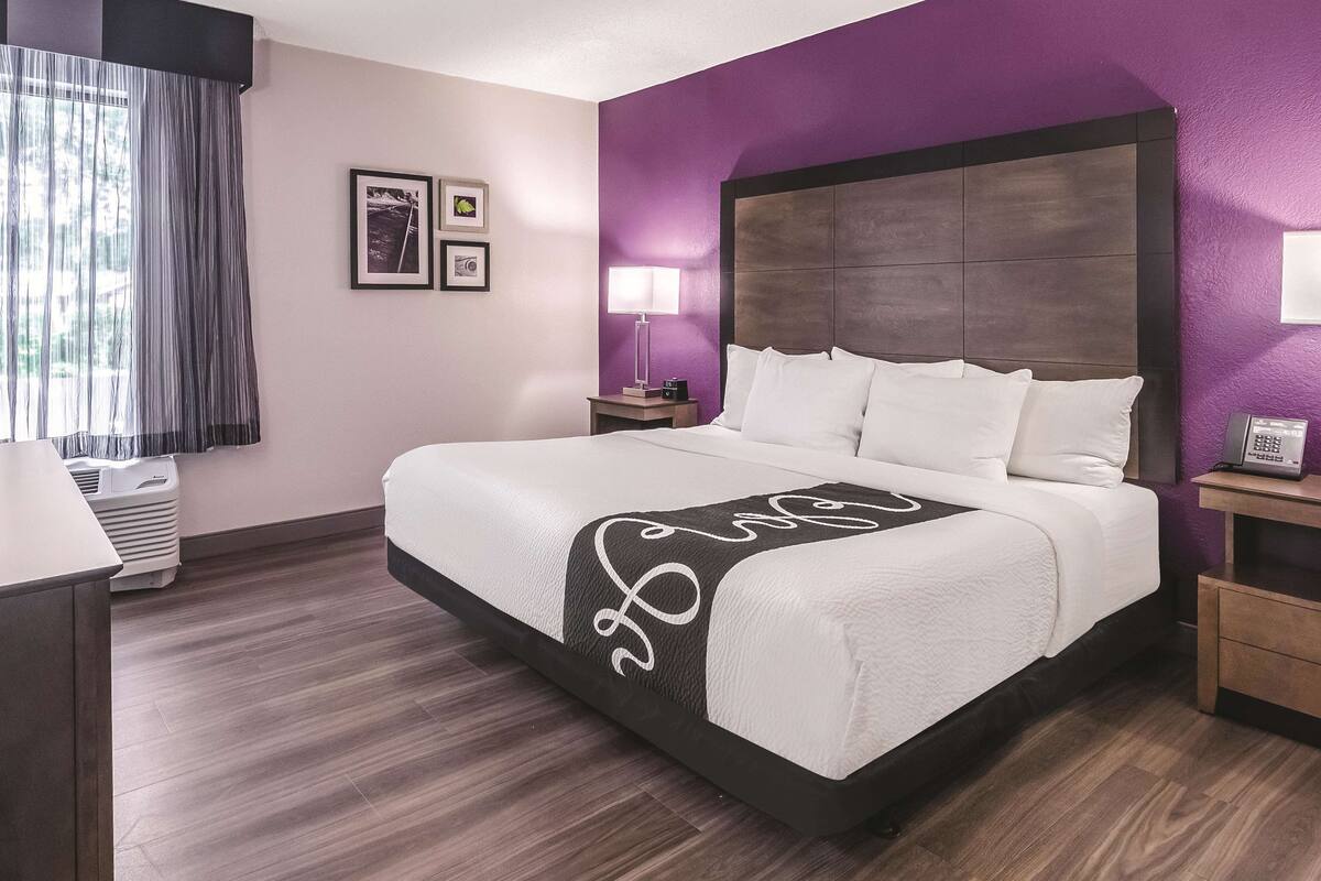 Hotelkamer met een groot bed, nachtkastje, lamp en een aan de muur bevestigde telefoon.