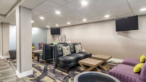 A modern hotel lobby with a sofa, armchairs, a coffee table, and a large TV mounted on the wall.