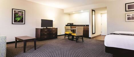 A hotel room with a bed, a desk, a chair, a dresser, and a television.