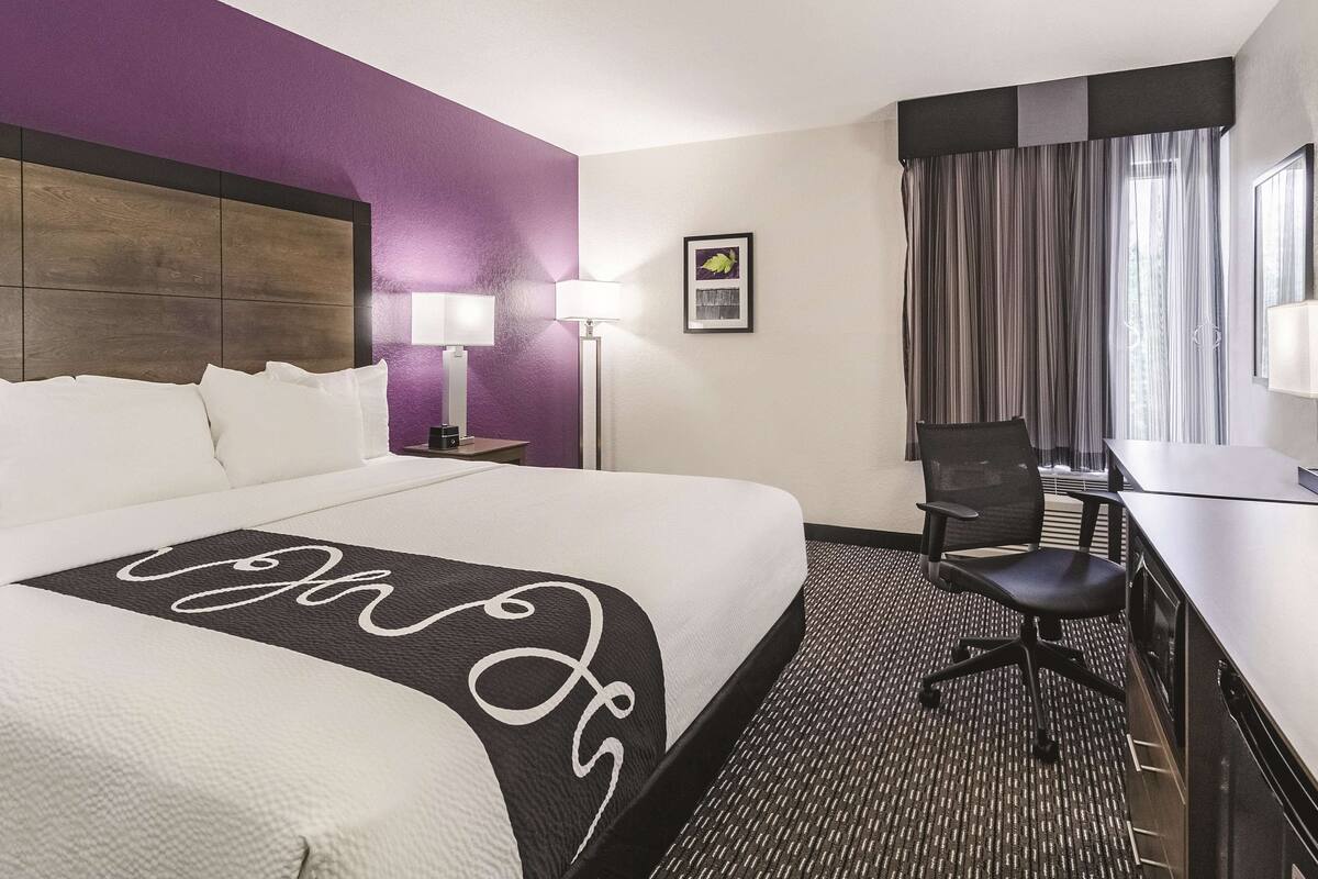 Een hotelkamer met een groot bed, een bureau, een stoel, een lamp en een schilderij aan de muur.