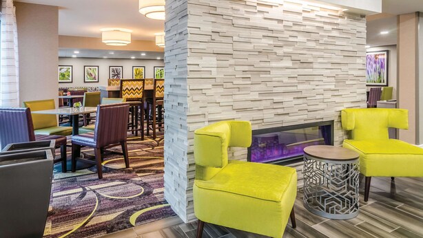 A modern hotel lobby with a seating area featuring yellow chairs, a patterned carpet, and a decorative wall with a geometric design.