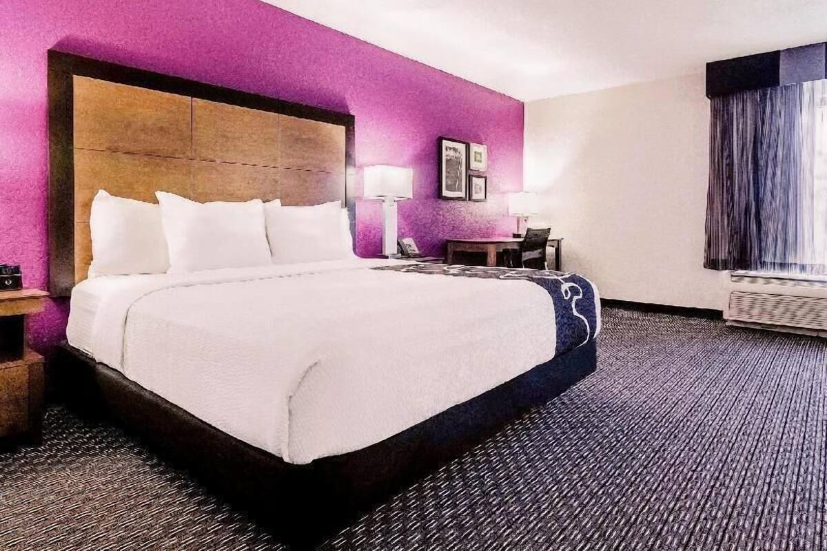Camera d'albergo con un letto grande, una testiera in legno, un comodino, una scrivania, una sedia, una lampada e una finestra con tende.