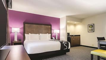 A hotel room with a bed, bedside tables, a desk, a chair, a kitchenette, and a bathroom.