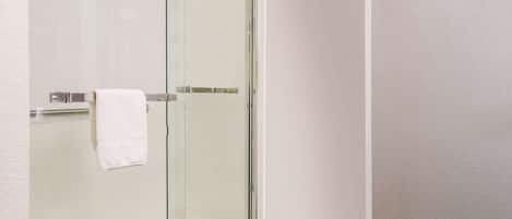 A modern bathroom with a glass shower enclosure, a white towel on the towel rack, and a wooden floor.