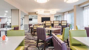 Zona de dinar d'un hotel modern, amb diverses taules i seients privats, una catifes amb dibuixos i una xemeneia central.
