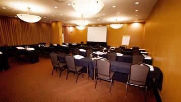 A conference room with multiple tables and chairs, a large screen, and a projector.