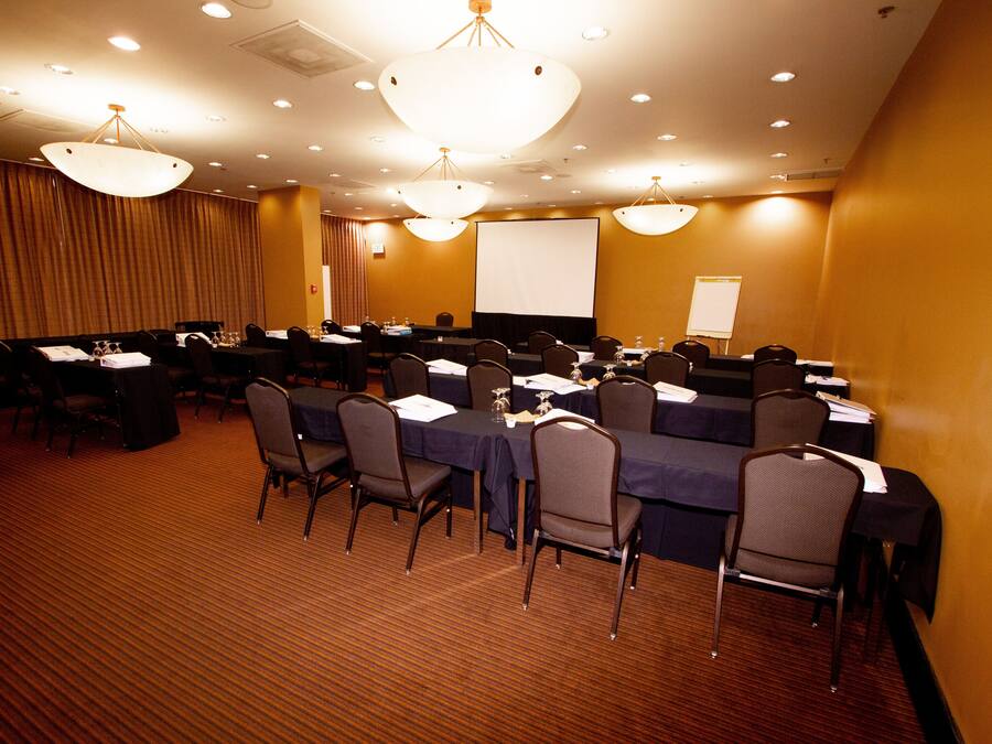 A conference room with multiple tables and chairs, a large screen, and a projector.
