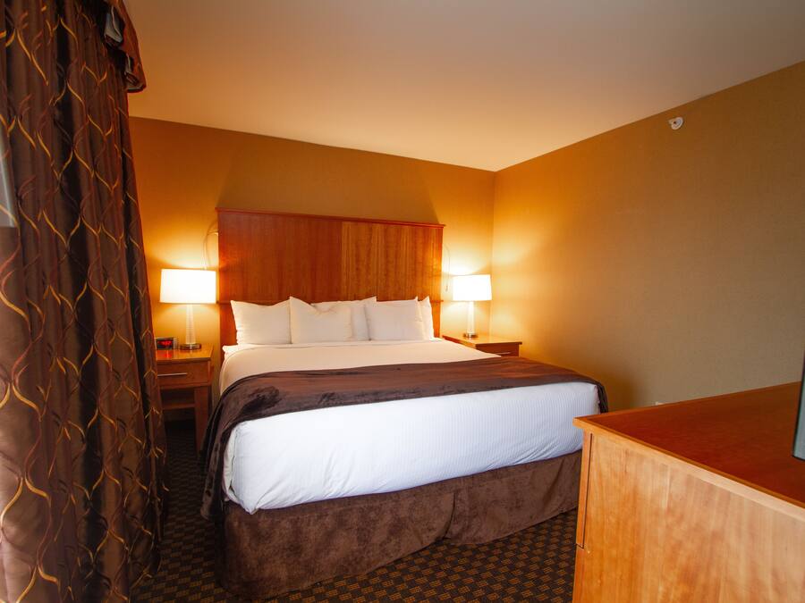 Een hotelkamer met een bed, twee bedlampen, een houten hoofdeinde, een televisie op een houten standaard en een gordijn met een patroon.