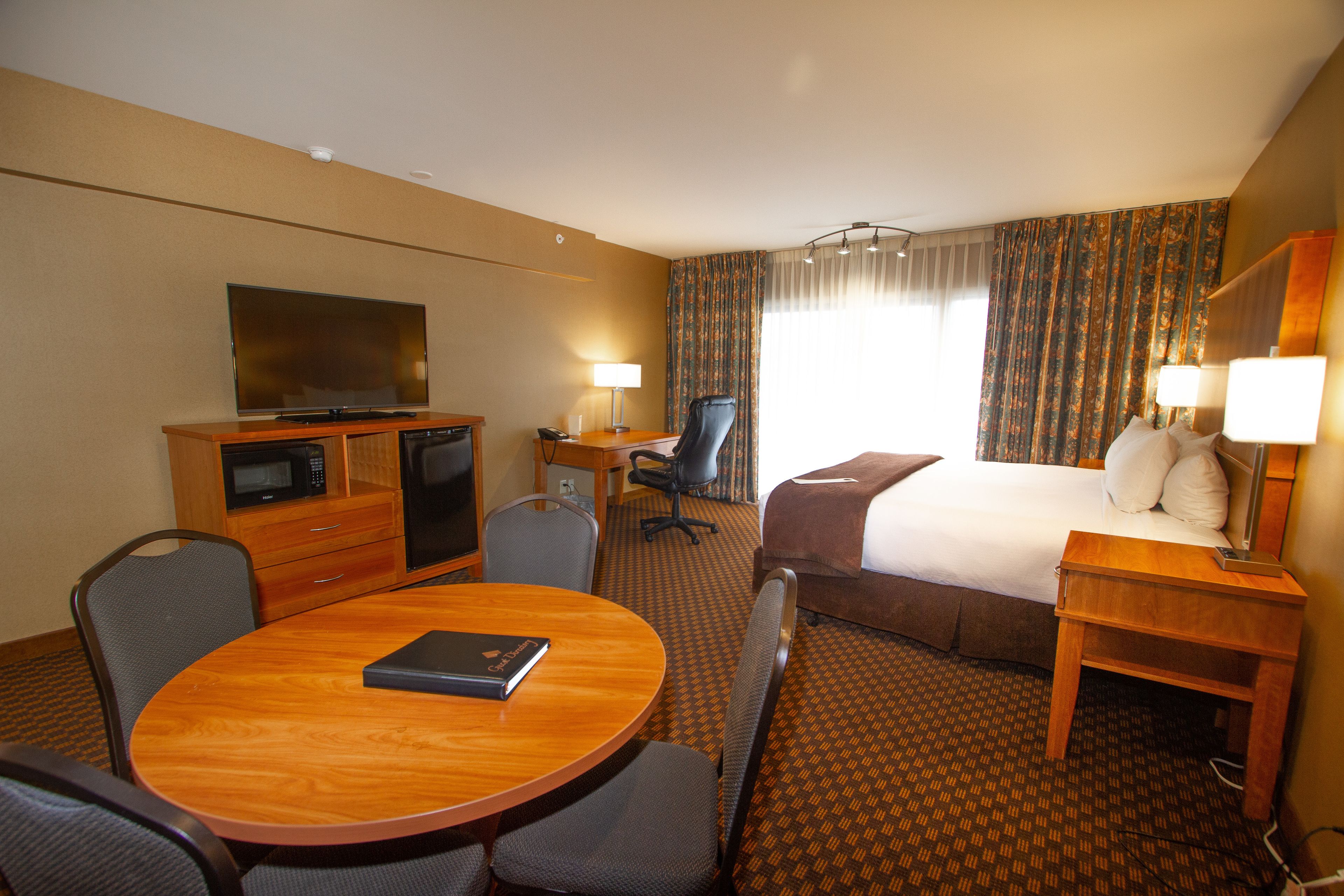 A hotel room with a bed, desk, chair, television, and a dining table.