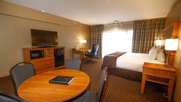A hotel room with a bed, desk, chair, television, and a dining table.