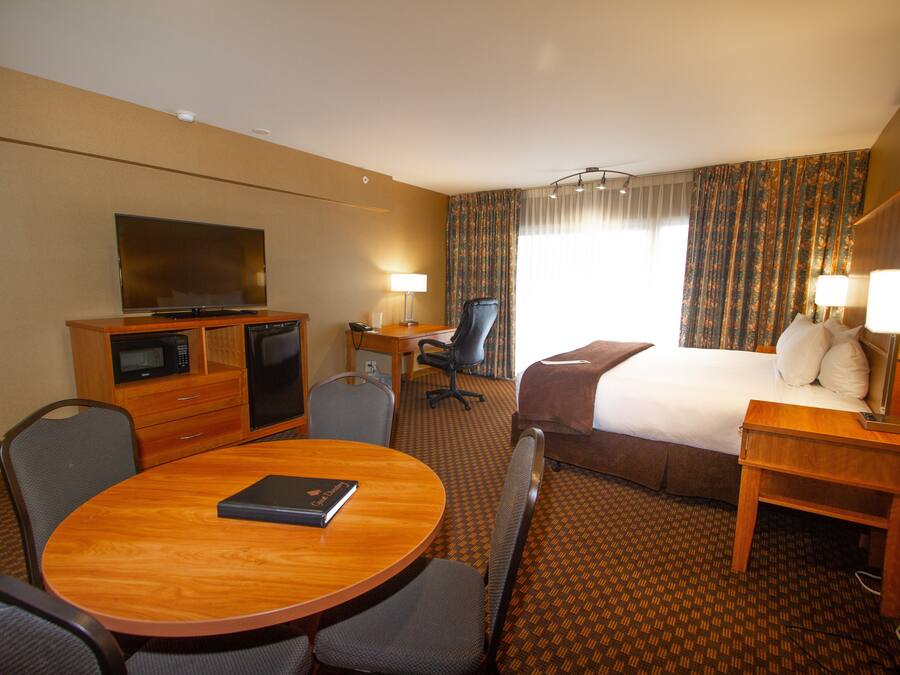 A hotel room with a bed, desk, chair, television, and a dining table.