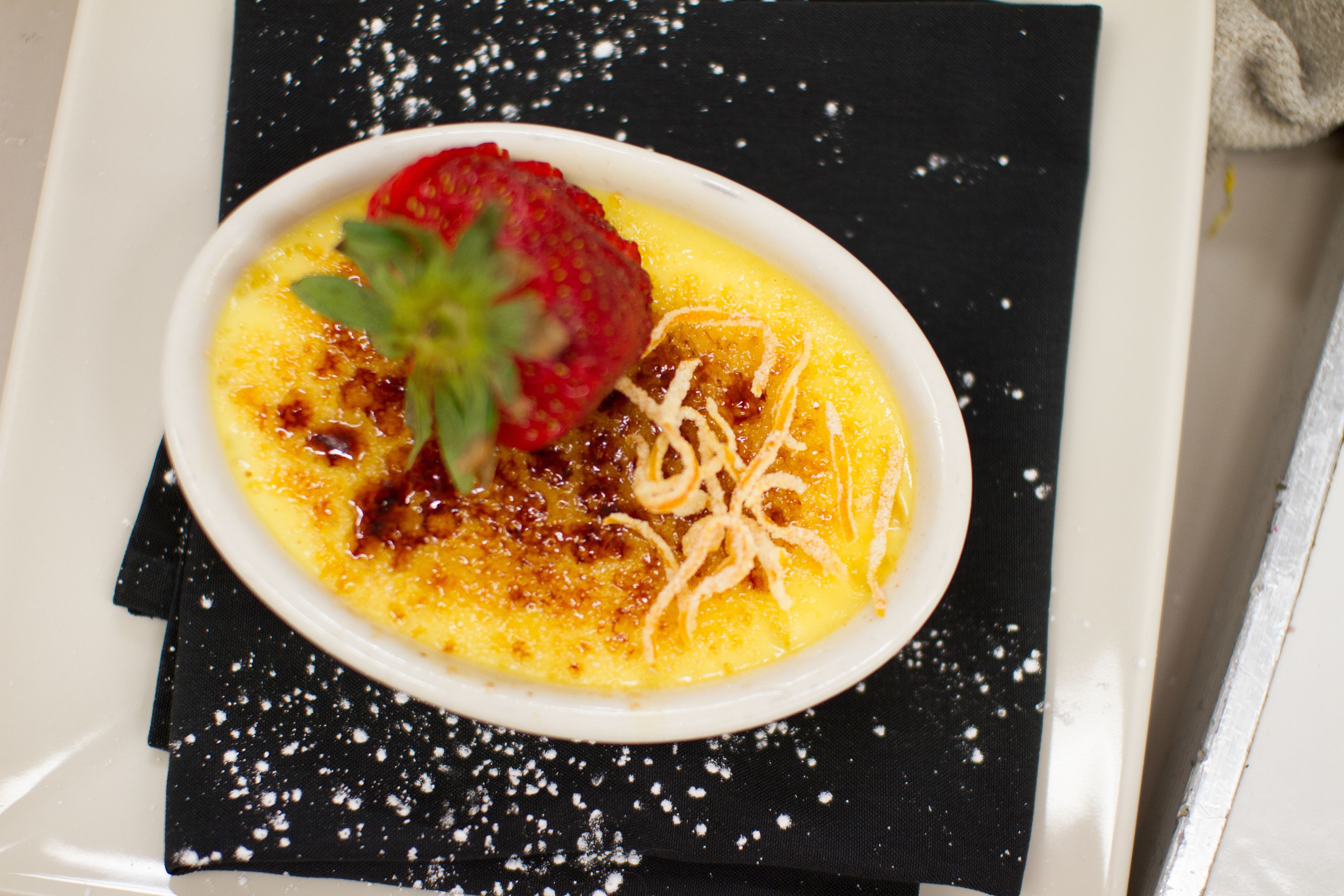 A dessert in a white bowl on a black napkin with powdered sugar.