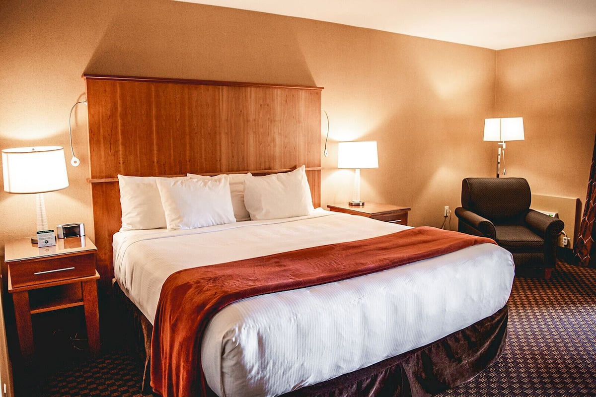 A hotel room with a large bed, two bedside tables, a chair, and two lamps.
