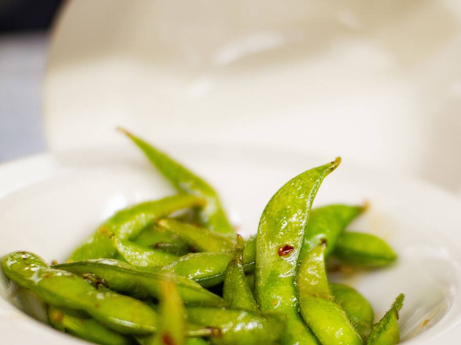 A white bowl filled with green edamame on a black surface.