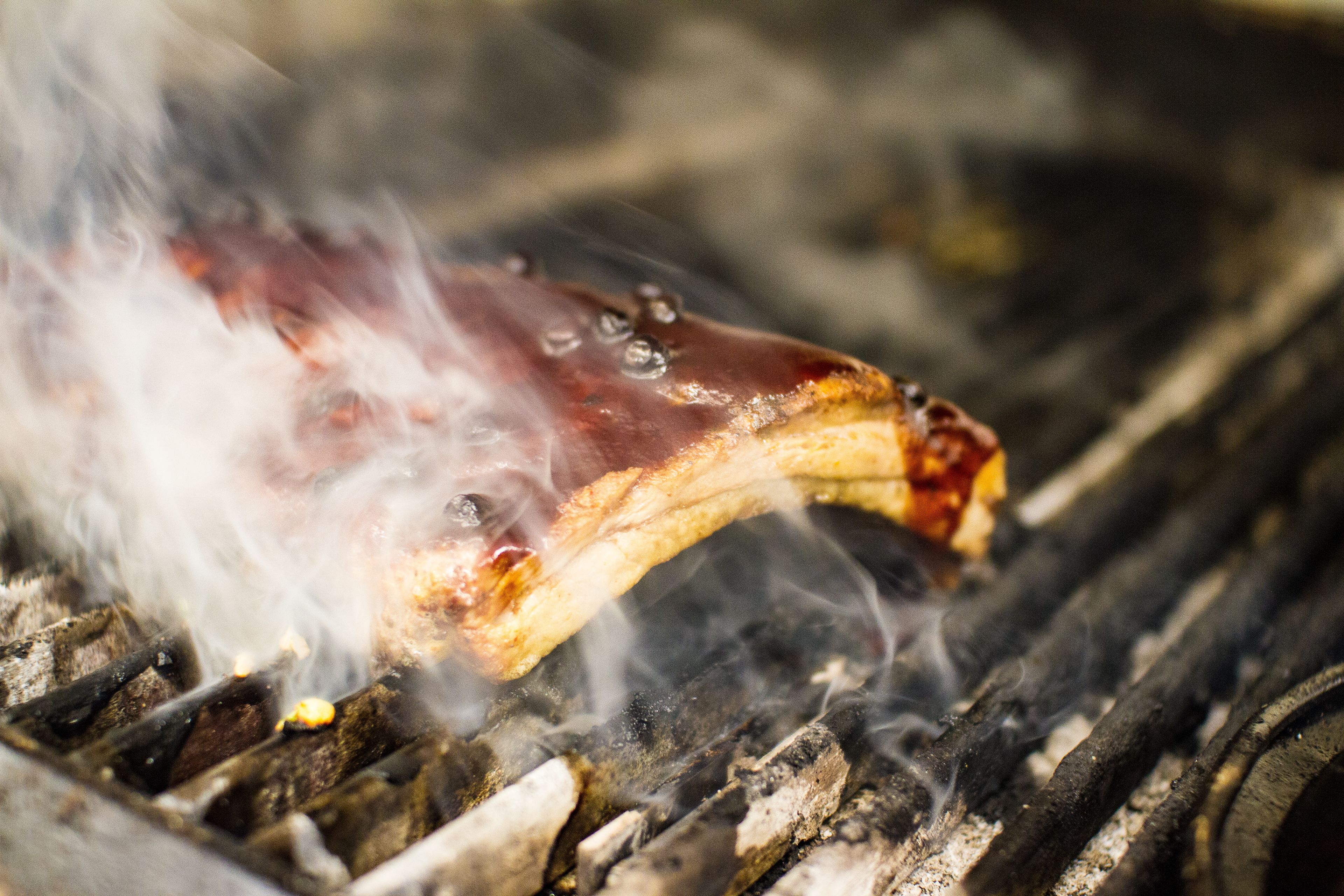 Close-up de carne grelhada com marcas de grelha e fumaça, indicando que está sendo preparada em brasa.