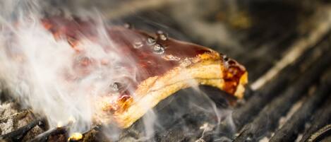 A close-up of a grilled meat with visible grill marks and smoke, indicating it is being cooked over an open flame.
