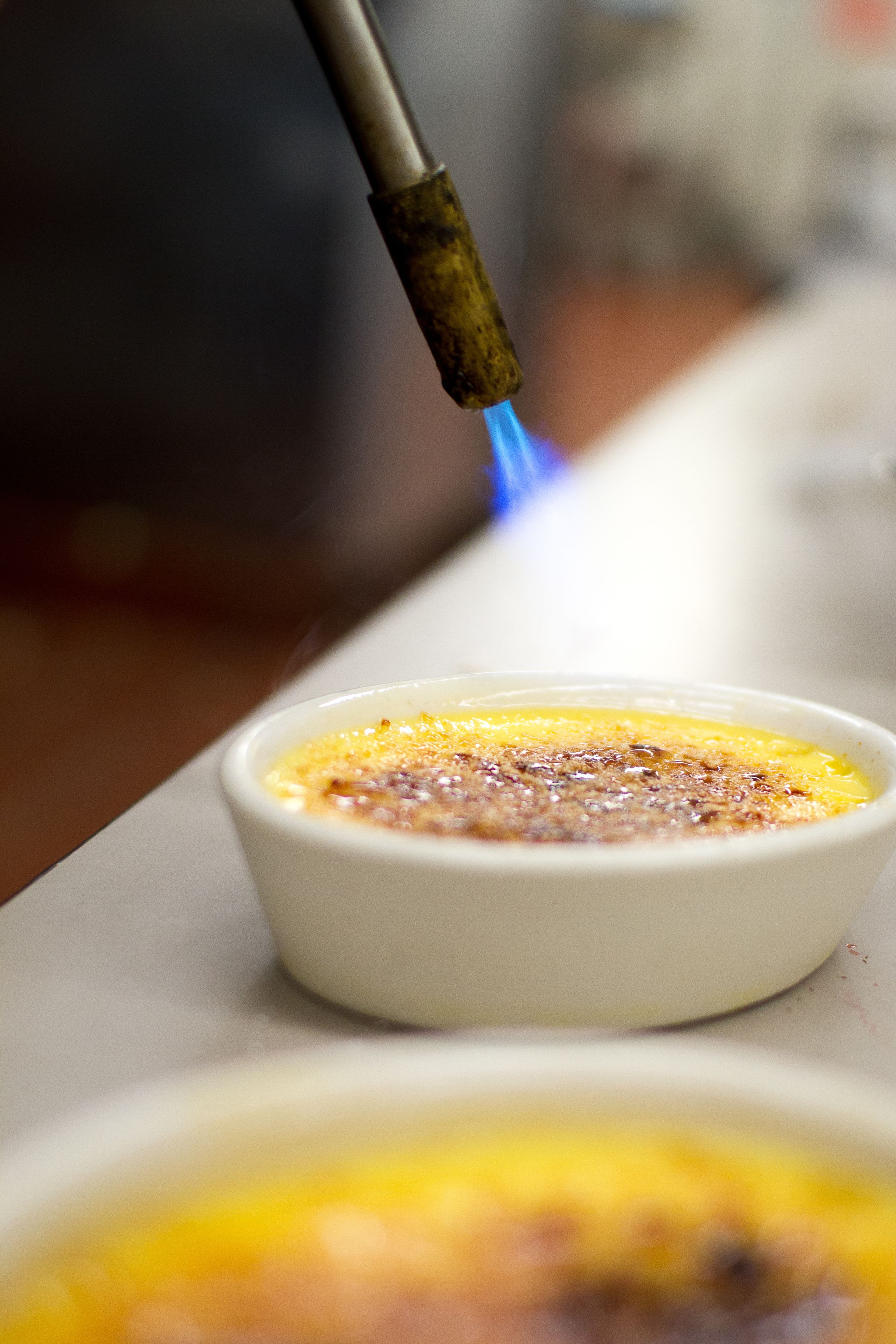 Gros plan d’une crème brûlée sur laquelle on utilise un chalumeau pour caraméliser la surface.