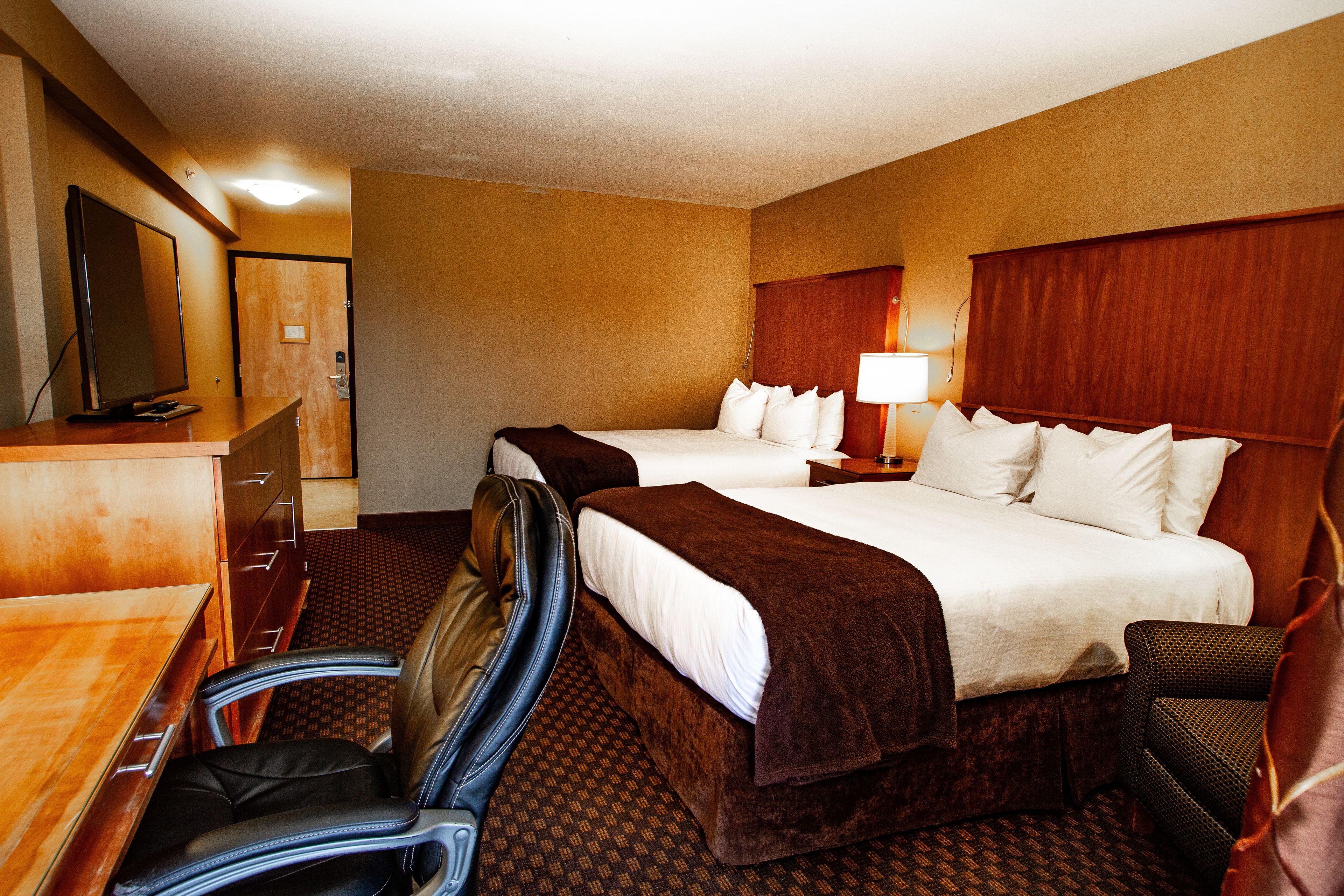 A hotel room with two beds, a desk with a chair, a TV, and a lamp.