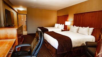 A hotel room with two beds, a desk with a chair, a TV, and a lamp.
