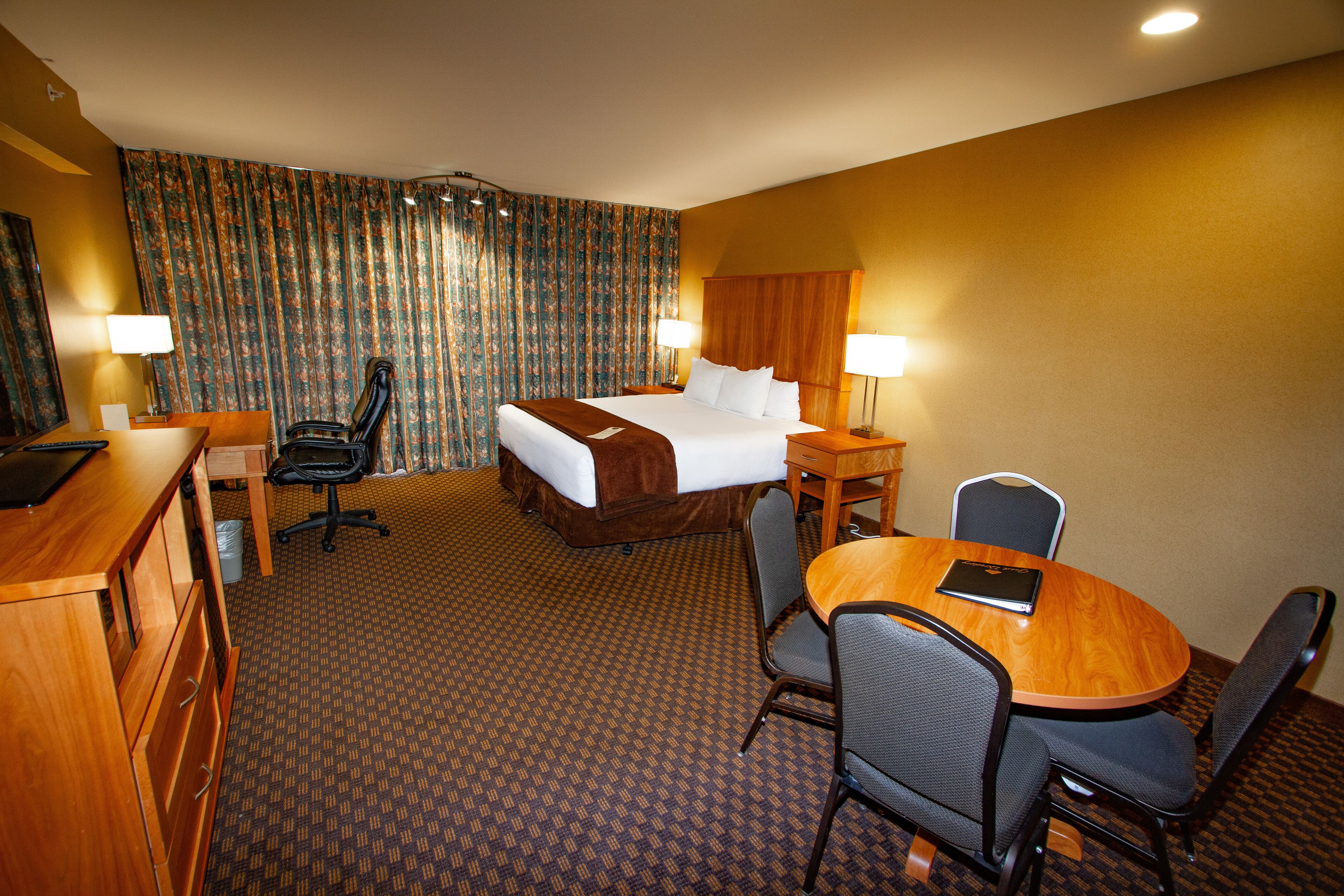 A hotel room with a bed, desk, chairs, and a small table.