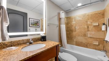 A bathroom with a granite countertop sink, a mirror, a toilet, and a bathtub.