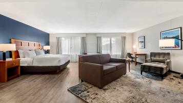 A hotel room with a bed, a sofa, a chair, a desk, and a lamp.