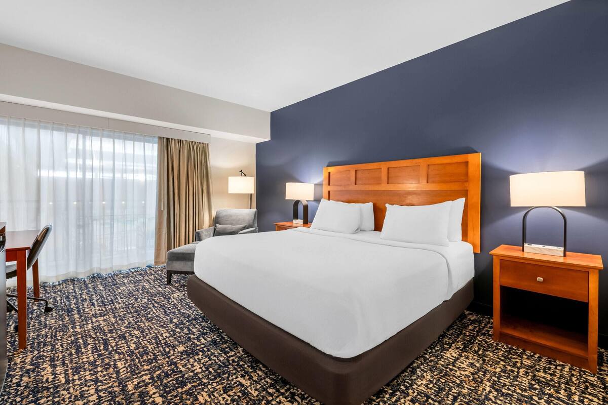 A hotel room with a large bed, two bedside tables with lamps, a desk, and a chair.